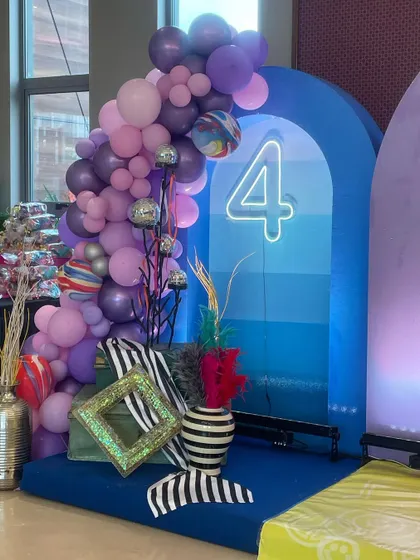 A vibrant and playful decor setup for a 4th birthday party. The mix of purple and blue balloons, a neon number '4', and quirky striped vases shows my creative and eclectic style.