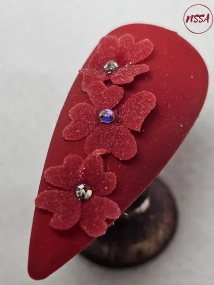A student's work on 3D velvet-texture floral nails. The deep red matte finish combined with the soft texture and crystal accents is a very advanced and beautiful technique.