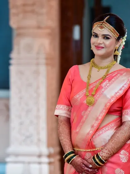 A poised portrait of the bride in her elegant pink wedding saree, standing against ornate architectural pillars.
