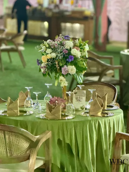 A close-up of a guest table, showing the elegant green velvet tablecloth, charger plates, and a beautiful floral centerpiece.