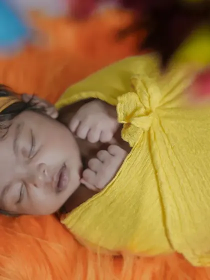 A close-up of a newborn wrapped in a sunny yellow cloth, adorned with a matching headband.
