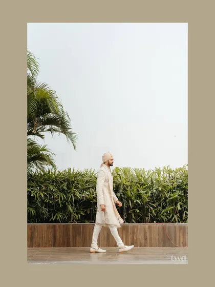 A candid walking shot of the groom in his elegant ivory sherwani. The motion captures a sense of purpose and grace as he makes his way to the ceremony.