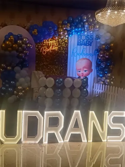 A clear view of the Boss Baby stage for Rudransh's party. The setup includes a gold shimmer backdrop, character cutouts, and large, bright marquee letters for his name.