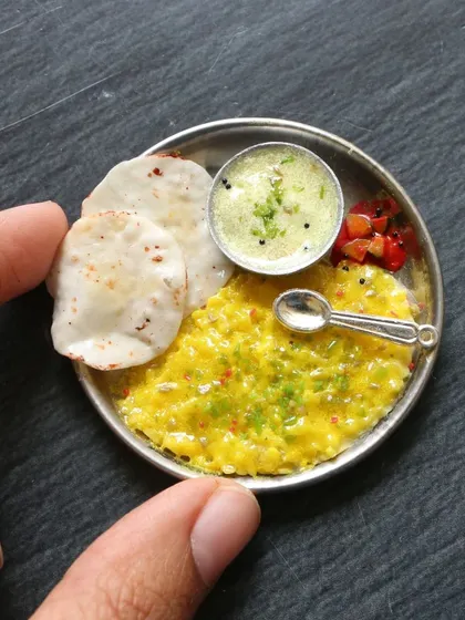 A cute miniature of khichdi and kadhi served on a tiny steel plate with papad.