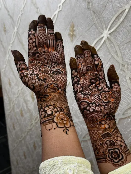 An intricate and dense bridal henna application for a fellow makeup artist. The design is packed with florals, paisleys, and fine-line details, covering the hands and extending up the arms.