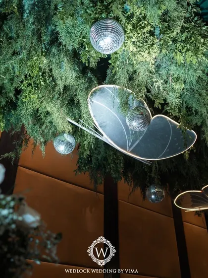 A walkthrough of a sangeet with an enchanted forest theme. The decor features a ceiling of lush greenery, sparkling disco balls, and glowing LED butterflies, creating a truly magical atmosphere.