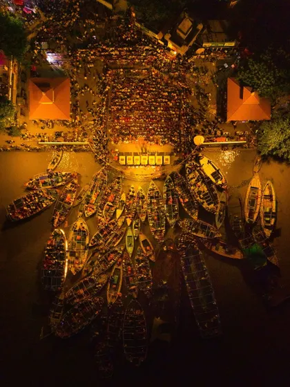 A top-down aerial view of the Ganga Aarti in Varanasi, capturing the spiritual gathering as a symphony of light. The boats filled with devotees and the priests on the ghat create a powerful image of collective faith, visible only from this unique vantage point.