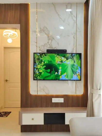 A close-up of a modern TV wall unit. The design combines a fluted wooden panel with a large marble-finish slab, creating a beautiful contrast of textures. The integrated backlighting adds warmth and highlights the materials.