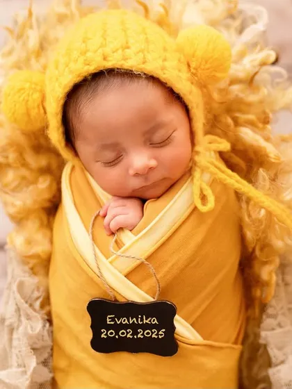 A close-up of a sleeping newborn in a yellow knit hat, with a little slate marking her birth date. These personalized details make your photos even more special.