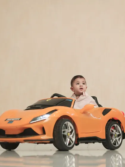 A future race car driver in the making. This little boy looks ready for action in his bright orange toy sports car.