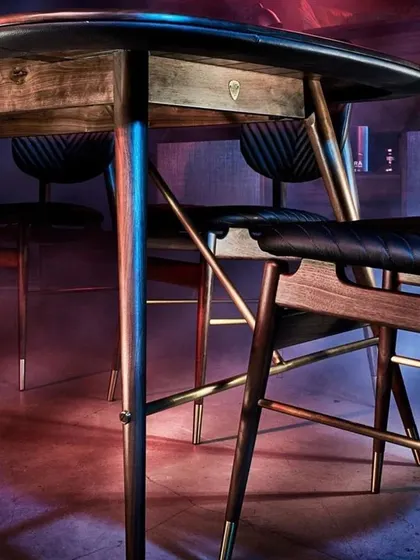 A dramatic shot of the Volta Dining Table, highlighting the sleek design of its legs and the rich texture of the walnut wood. This is furniture that defies convention and makes a confident statement.