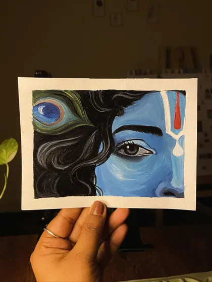 Holding the small Krishna painting, showing its size and vibrant colors.