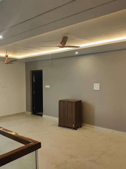 A view of the upper floor living area in a newly completed residence. The space features clean lines, recessed ceiling lights, and a glass railing overlooking the floor below, creating a sense of openness.