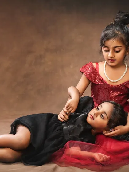A story of sisterly love. One sister in a red dress comforts her younger sister, who is lying in her lap. A touching and artistic portrait.