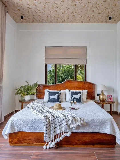A beautifully styled shot of the guest bedroom, featuring a custom wooden bed with a curved headboard and a ceiling covered in a subtle textured wallpaper, adding a rustic touch.