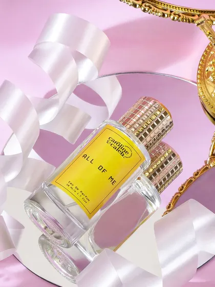 A celebratory and feminine perfume shot, using ribbons and mirrors against a pink background. The composition is dynamic and luxurious, perfect for a fragrance named 'All of Me'.