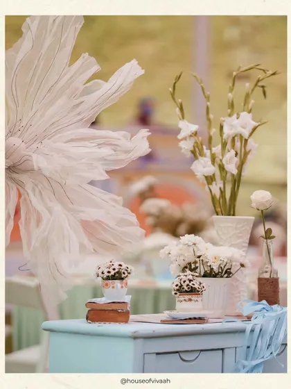 A detail shot of a tablescape, featuring a giant ethereal paper flower and simple arrangements in textured vases, adding an artistic and delicate touch to the Haldi lunch.