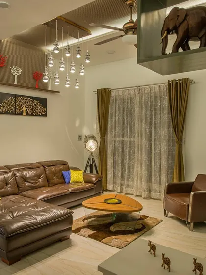 Another view of the living space, highlighting the interplay of different decor elements. A tripod floor lamp adds an industrial touch, while the custom coffee table and shelving with elephant sculptures bring in unique, personal details.