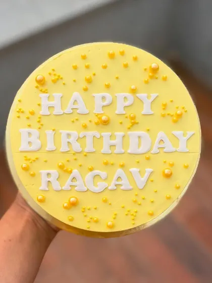 A cheerful yellow birthday cake with white lettering and yellow pearl sprinkles.