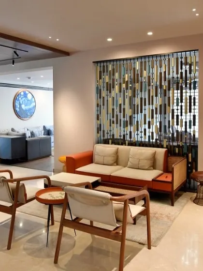 A casual seating area featuring mid-century modern inspired chairs and a vibrant orange sofa. A decorative screen made of wood and metal adds texture and visual interest while subtly dividing the space.