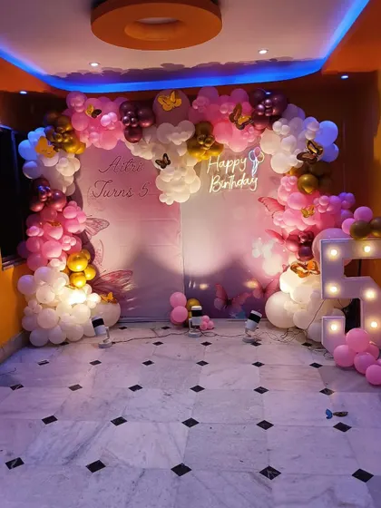 A beautiful butterfly and fairy theme for a 5th birthday, using a soft pink and white color palette, a large balloon arch, and a light-up marquee number.