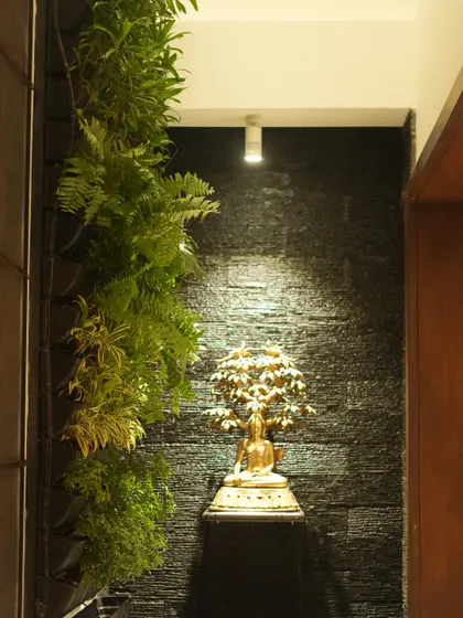 We create tranquil corners by blending nature with art. This vertical garden is paired with a spotlit Buddha statue against a dark, textured wall, creating a focal point of peace and serenity in a modern hallway.