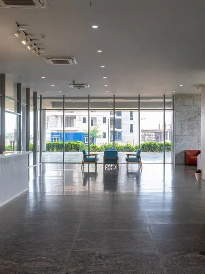 The spacious, minimalist lobby of the Pinnacle Campus, with floor-to-ceiling windows that flood the space with natural light. The textured concrete wall adds a tactile quality, while the open layout provides a clear view of the landscaped exterior.