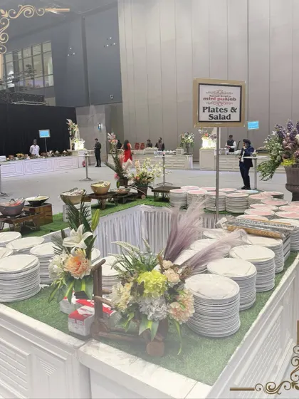 An elegant plates and salad station at a large indoor event. The floral arrangements and clean, white setup create a fresh and inviting look.