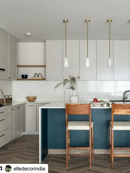 In the Neutral Chic home, the kitchen features a large island with a pop of deep blue. Herringbone wood-look tiles on the floor add texture and warmth, while pendant lights provide focused task lighting.