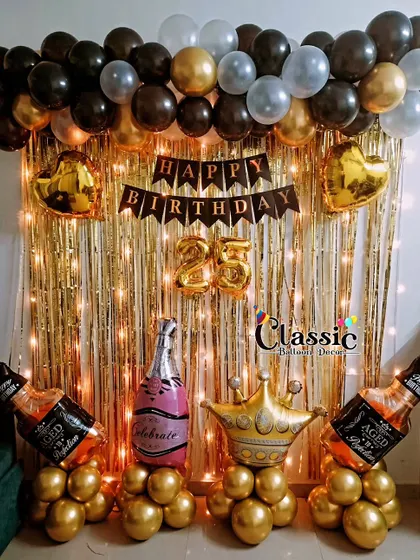 A fun 'Cheers' theme for a 25th birthday home party, with a gold shimmer curtain, fairy lights, and champagne and whiskey bottle foil balloons.