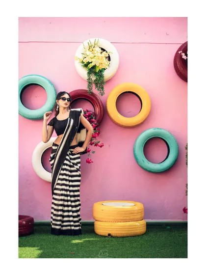 Bold and beautiful. The contrast of the striped saree against the colorful, quirky background of painted tires makes for a fun, modern, and high-impact fashion portrait.