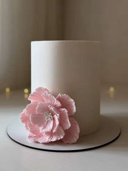 A clean and simple white cake with a single, large, handcrafted pink wafer paper flower. This is a perfect example of minimalist elegance.