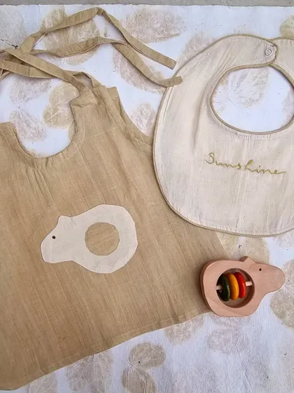 This neutral-toned newborn gift set is perfect for any baby. It includes a hand-dyed kora cotton top with a bear applique, a bib, and a matching Channapatna bear rattle, all made with natural and safe materials.