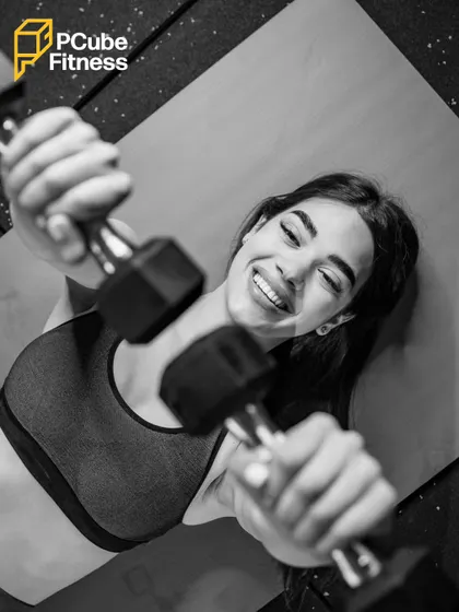 A woman smiles while doing a dumbbell floor press, showing that you can find joy in the journey to becoming stronger.