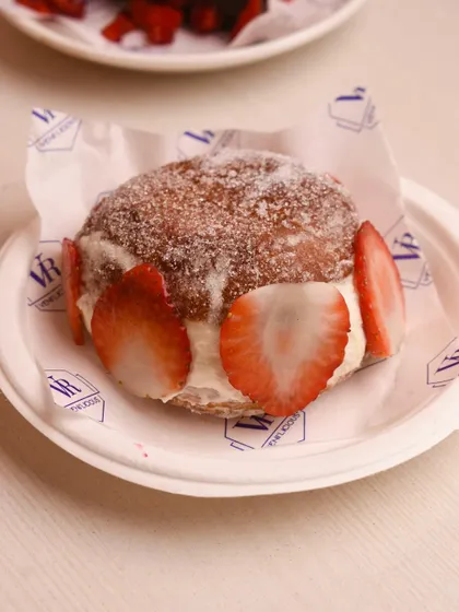 A close-up of the Strawberry Berliner. You can see the fresh cream and sliced strawberries nestled inside the soft, sugar-dusted dough.