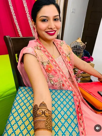 A smiling client showing a close-up of her forearm design, which features a beautiful peacock and dome motif.