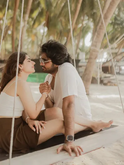 An intimate moment on a beach swing, capturing the couple's close connection and the beautiful texture of the surrounding palm trees.
