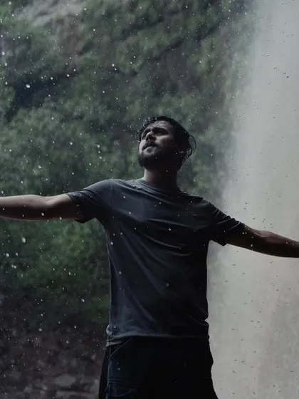 Photos of me embracing the monsoon, standing with arms outstretched in front of a waterfall and sitting contemplatively on a rock. These images convey a deep connection with nature.
