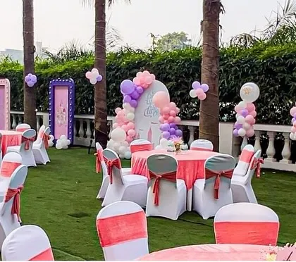 A wide shot of the outdoor princess party venue. The pink and white table settings, balloon columns, and themed backdrops come together to create a cohesive and enchanting environment.