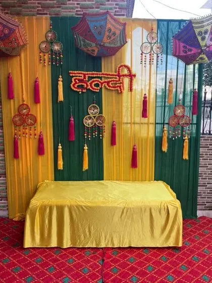 An outdoor Haldi seating area with a backdrop of yellow and green drapes, decorated with hanging tassels and dreamcatchers.