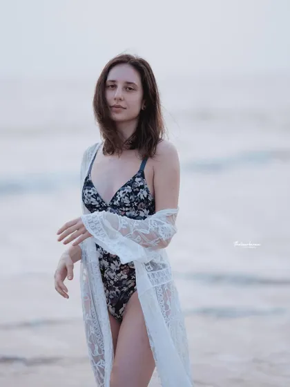 A full-length shot of the model in a swimsuit and lace robe, capturing a candid and natural moment on the beach.