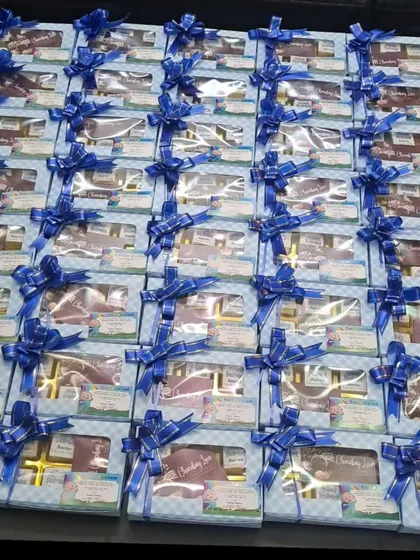 A bulk order of six-piece chocolate boxes for a Cocomelon-themed first birthday. The blue checkered pattern and matching ribbon were customized for the baby boy's party.