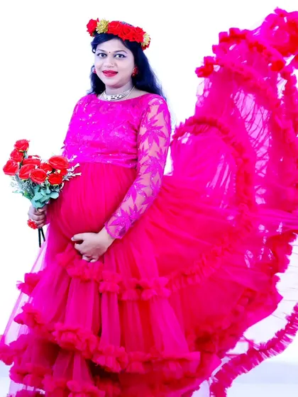 A joyful portrait of an expectant mother in a vibrant pink ruffled gown, holding a bouquet of red roses.