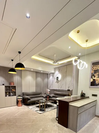 A dynamic living room design featuring a multi-level ceiling with a mix of straight and curved lines, cove lighting, and pendant lights. A small bar counter adds another layer of functionality.