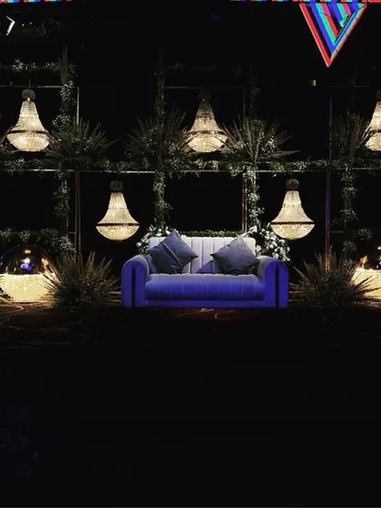 A unique stage design for an engagement, featuring a comfortable sofa set against a backdrop of greenery and nine suspended crystal chandeliers.