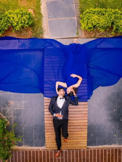 A unique aerial perspective of a couple lying on a wooden deck, with the blue gown spread out like wings. This drone shot is a perfect example of a creative and modern pre-wedding photo.