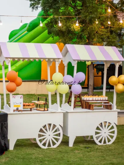 Food and dessert carts at a jungle-themed party. The carts have striped awnings and are placed outdoors, with a large bouncy castle visible in the background, promising a day of fun.