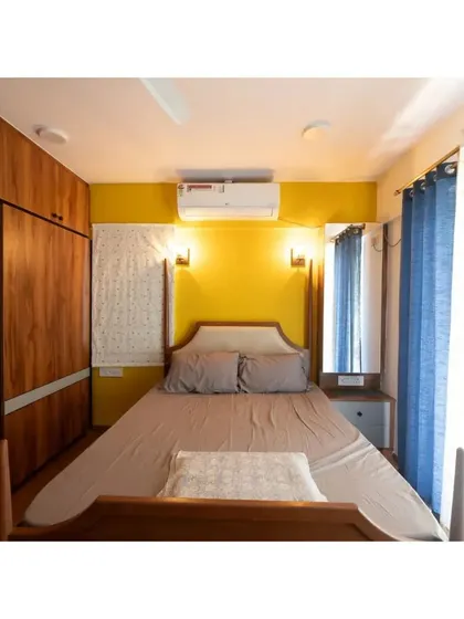 A cozy bedroom with a four-poster bed set against a vibrant yellow accent wall. The design balances warm wood tones with bright, cheerful color.