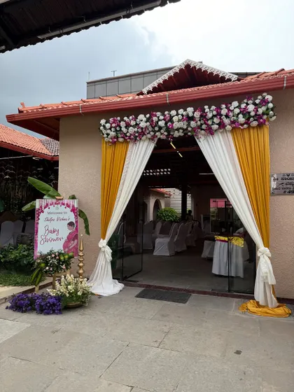The entrance to a baby shower hall, decorated with yellow and white drapes and a floral arch.