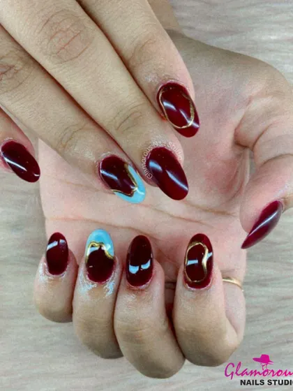 A rich and luxurious color combination. This set features deep, glossy maroon nails, with accent nails showcasing an abstract mix of light blue and gold for a truly artistic and high-fashion look.